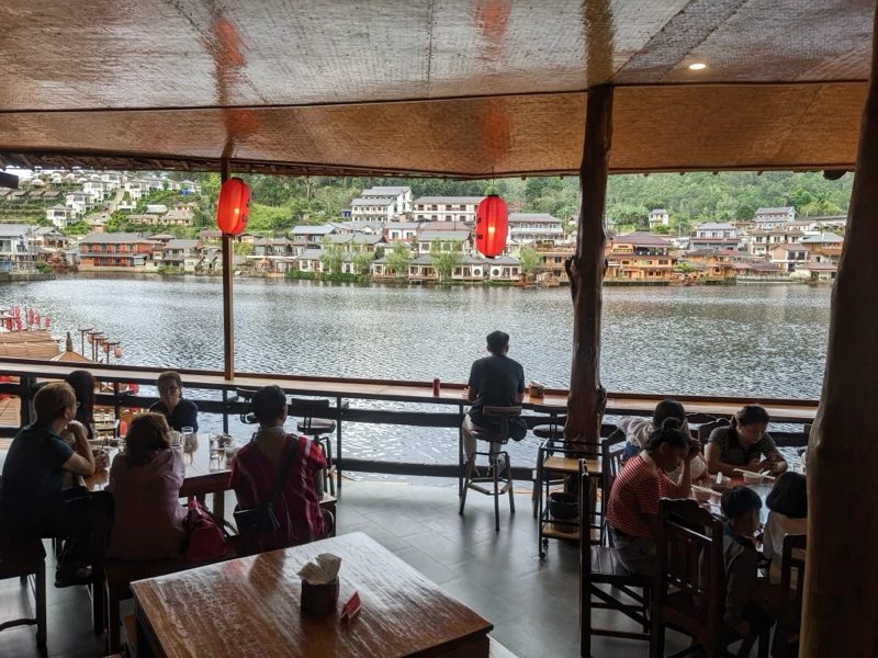 湖畔のレストランで食事をする人々、背景に町並みと湖